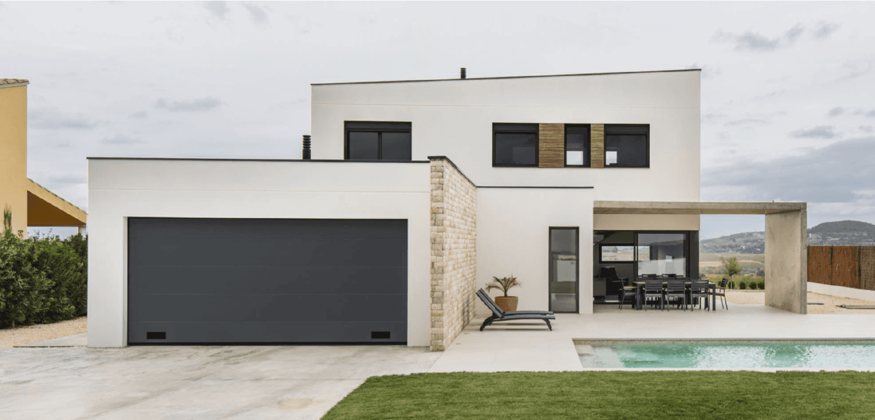 Modern white house with sleek design, large windows, pool, and patio furniture in the backyard.